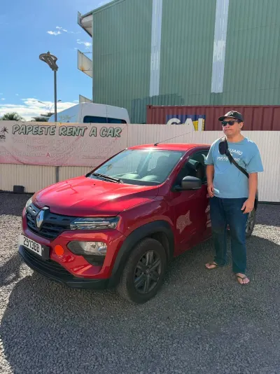 Client devant une Renault Kwid rouge, banderole Papeete Rent a Car